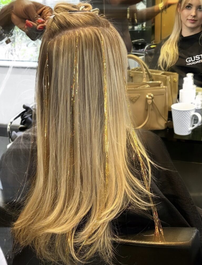 Gold hair tinsel woven through long blonde hair in the chair at Gusto Hair, London