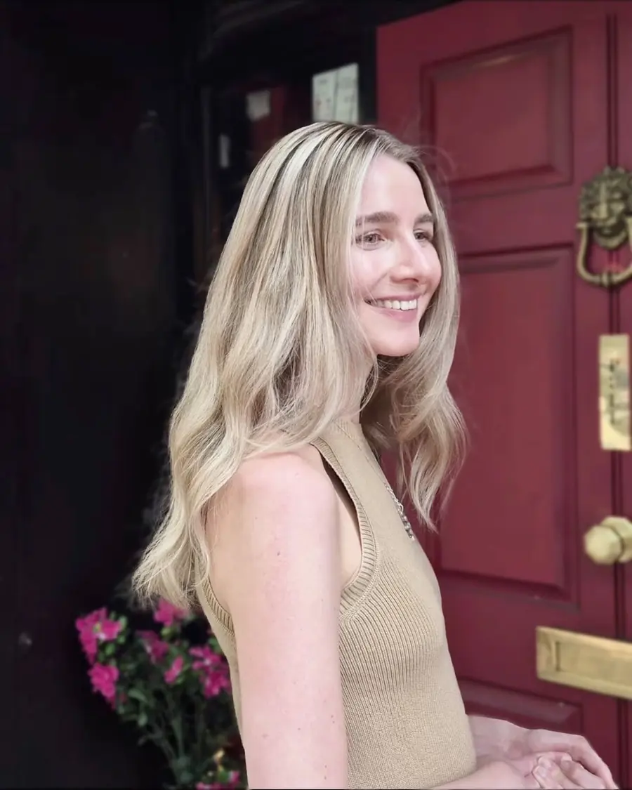 Long blonde balayage in soft waves, smiling outside a red front door